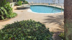 Une piscine entourée de verdure, un palmier et un bâtiment doté de balcons.