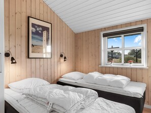Ein Zimmer mit zwei Betten, Holzwänden, einem gerahmten Bild und einem Fenster mit Blick.