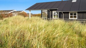 Una casa moderna con techo oscuro, ventanas grandes y un primer plano con césped.