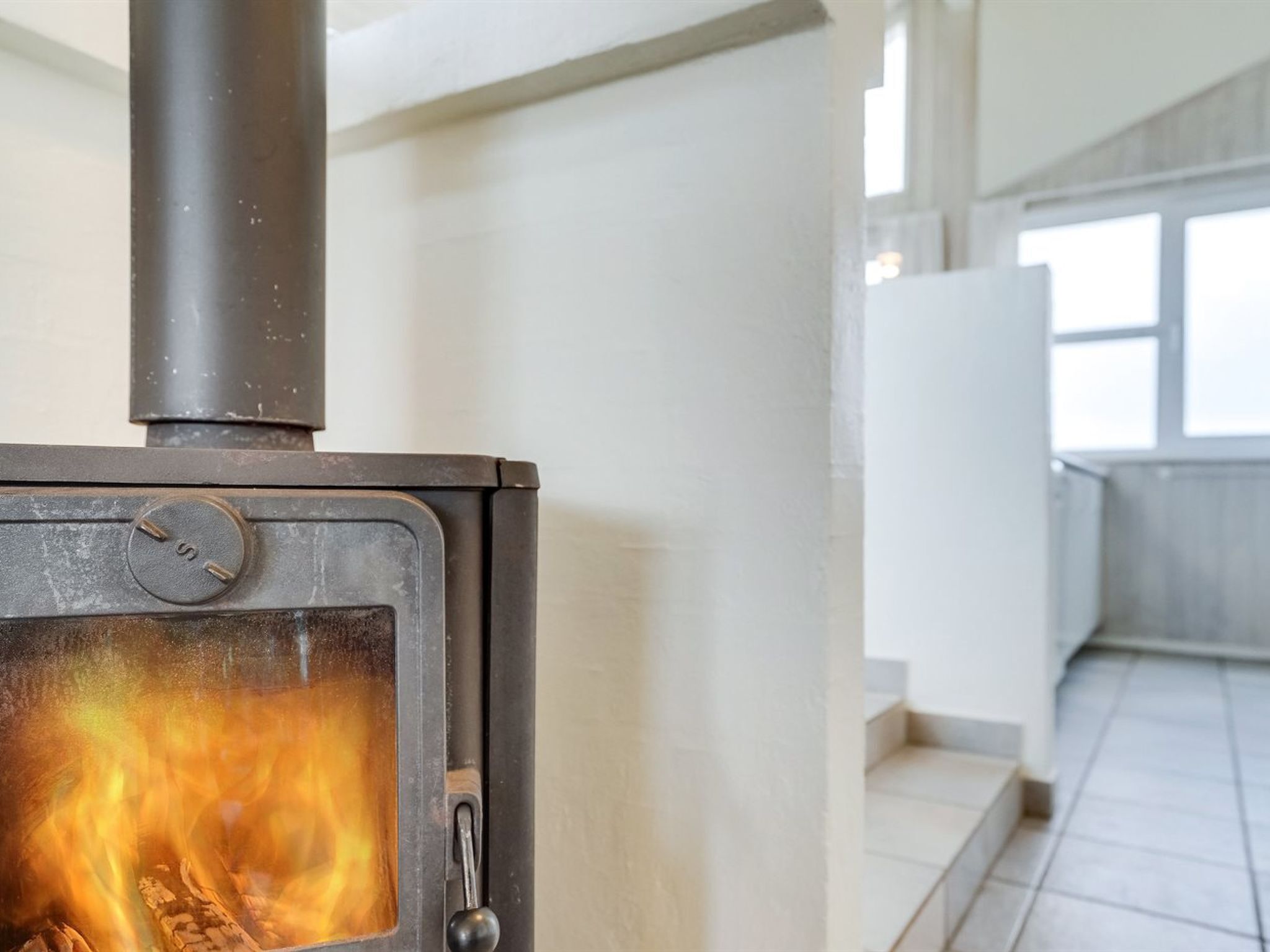En modern inredning med en vedeldad kamin, vita väggar och ett kaklat golv.