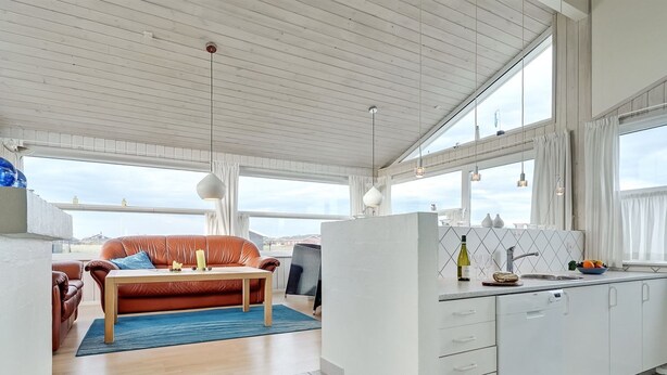 Un salon moderne avec un canapé en cuir, une table basse et un coin cuisine doté de meubles blancs et d’un évier.