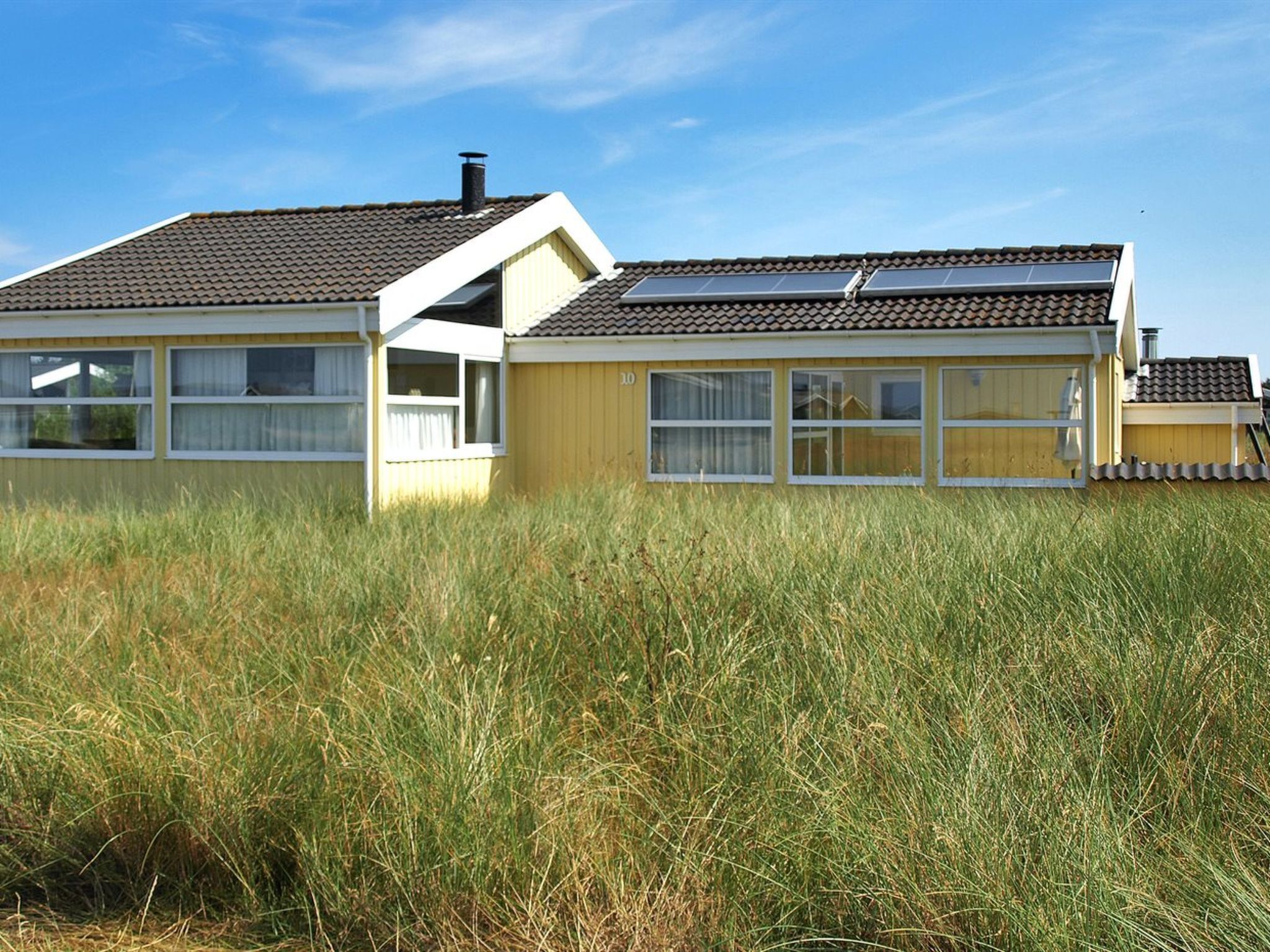 Ein zweistöckiges Haus mit einem geneigten Dach, großen Fenstern und einem Schornstein.