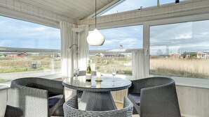 Un coin repas avec une table ronde et des chaises en osier, de grandes fenêtres donnant sur le paysage et un luminaire suspendu.