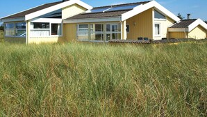 Une maison à deux étages, dotée d’un toit plat, de grandes fenêtres et d’un champ verdoyant au premier plan.