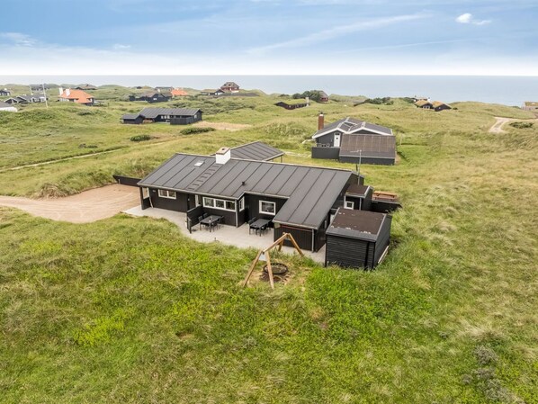 Une maison moderne dotée d’un grand patio, entourée de champs verdoyants et d’autres maisons en arrière-plan.