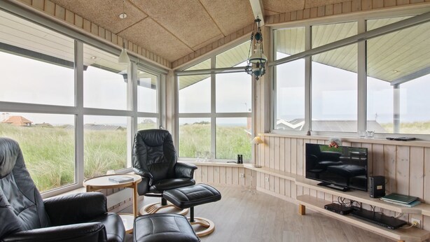Une pièce spacieuse avec de grandes fenêtres, un coin salon confortable avec un fauteuil et un pouf en cuir, une télévision et un plancher en bois.