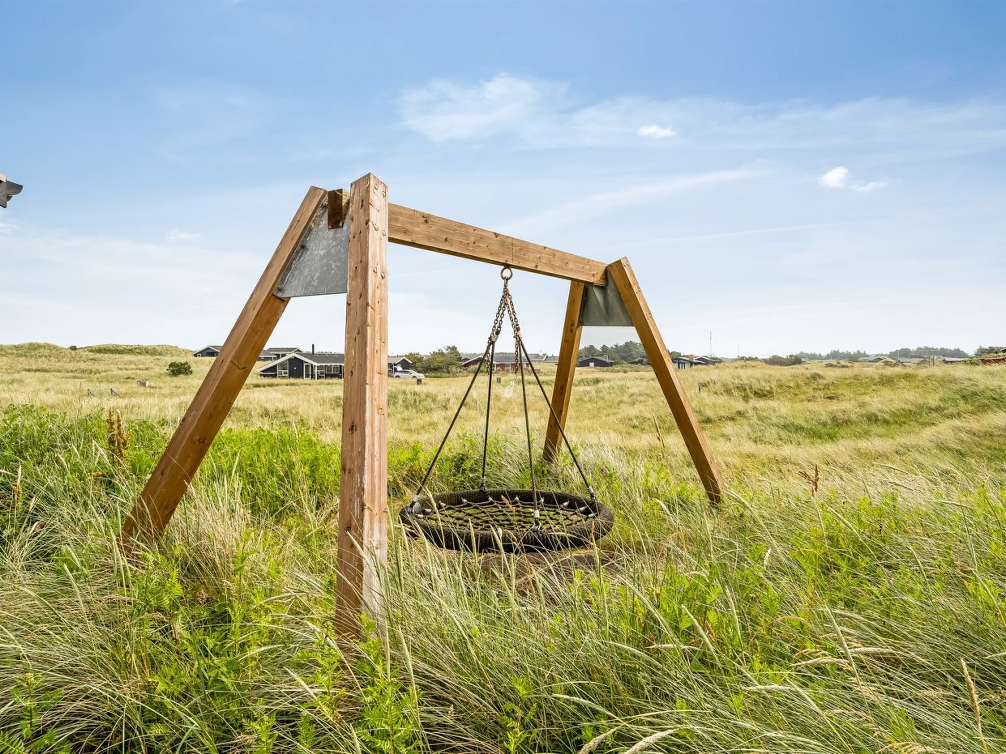 Een houten schommelset in een grasveld, met huizen op de achtergrond.
