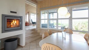 Un intérieur moderne avec une cheminée, de grandes fenêtres, un coin repas et un escalier.