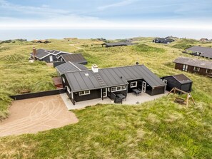 Une maison moderne avec un toit plat, entourée de dunes verdoyantes et offrant une vue dégagée sur la mer.