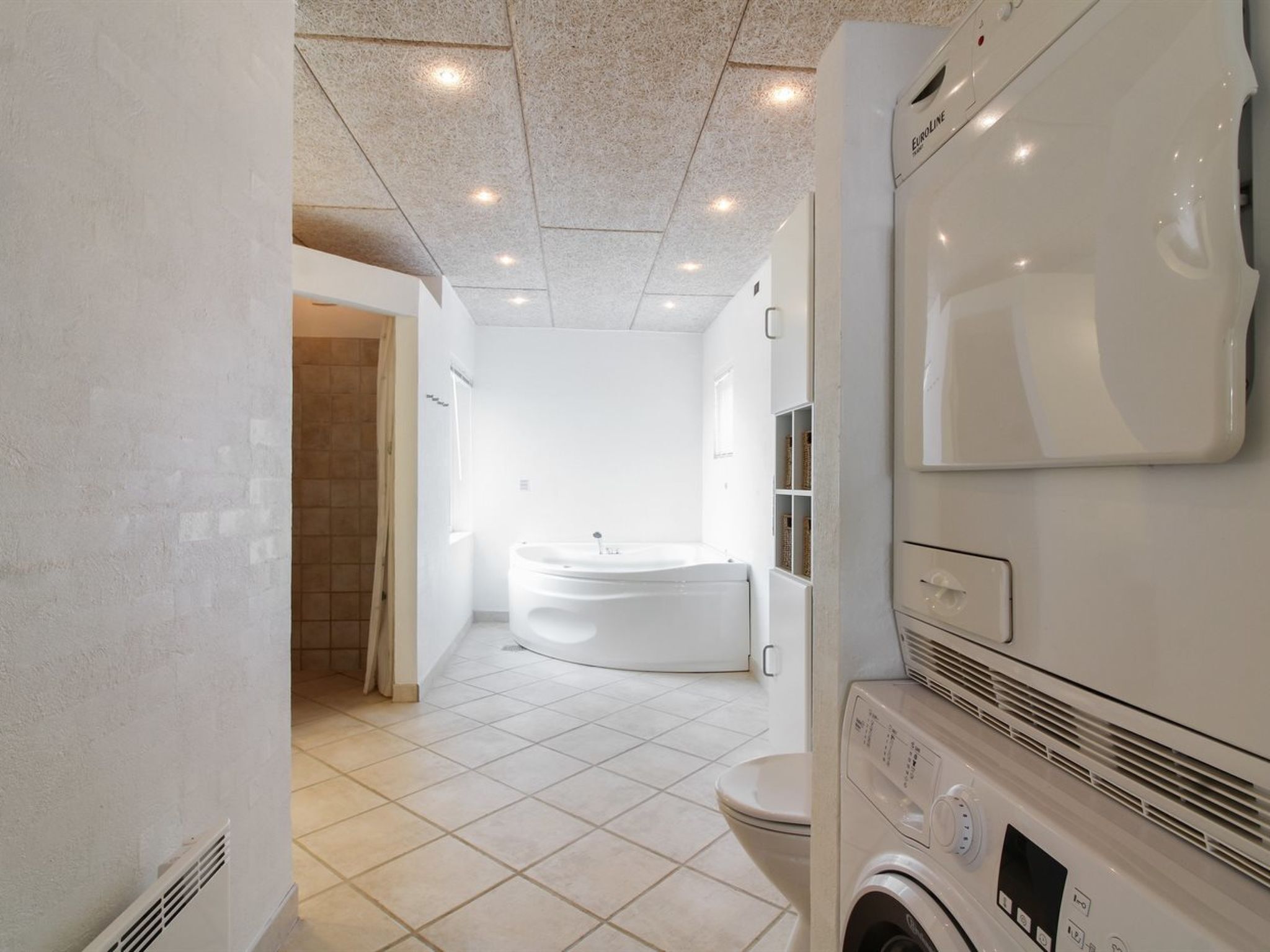 Une salle de bain moderne équipée d’un lave-linge intégré, d’une grande baignoire et de toilettes.