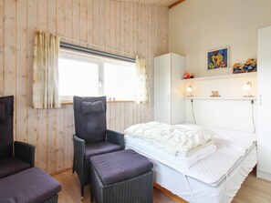 Une pièce comprenant un lit, une chaise, une petite table et une fenêtre avec des rideaux.