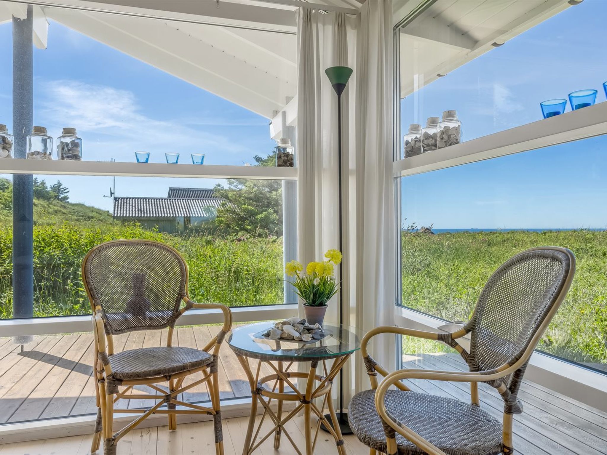 Un balcon avec des fauteuils en osier, une table en verre et une vue sur l’océan.