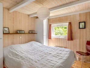 Une chambre à coucher avec un lit, une fenêtre avec des rideaux, une chaise et une étagère avec des photos.