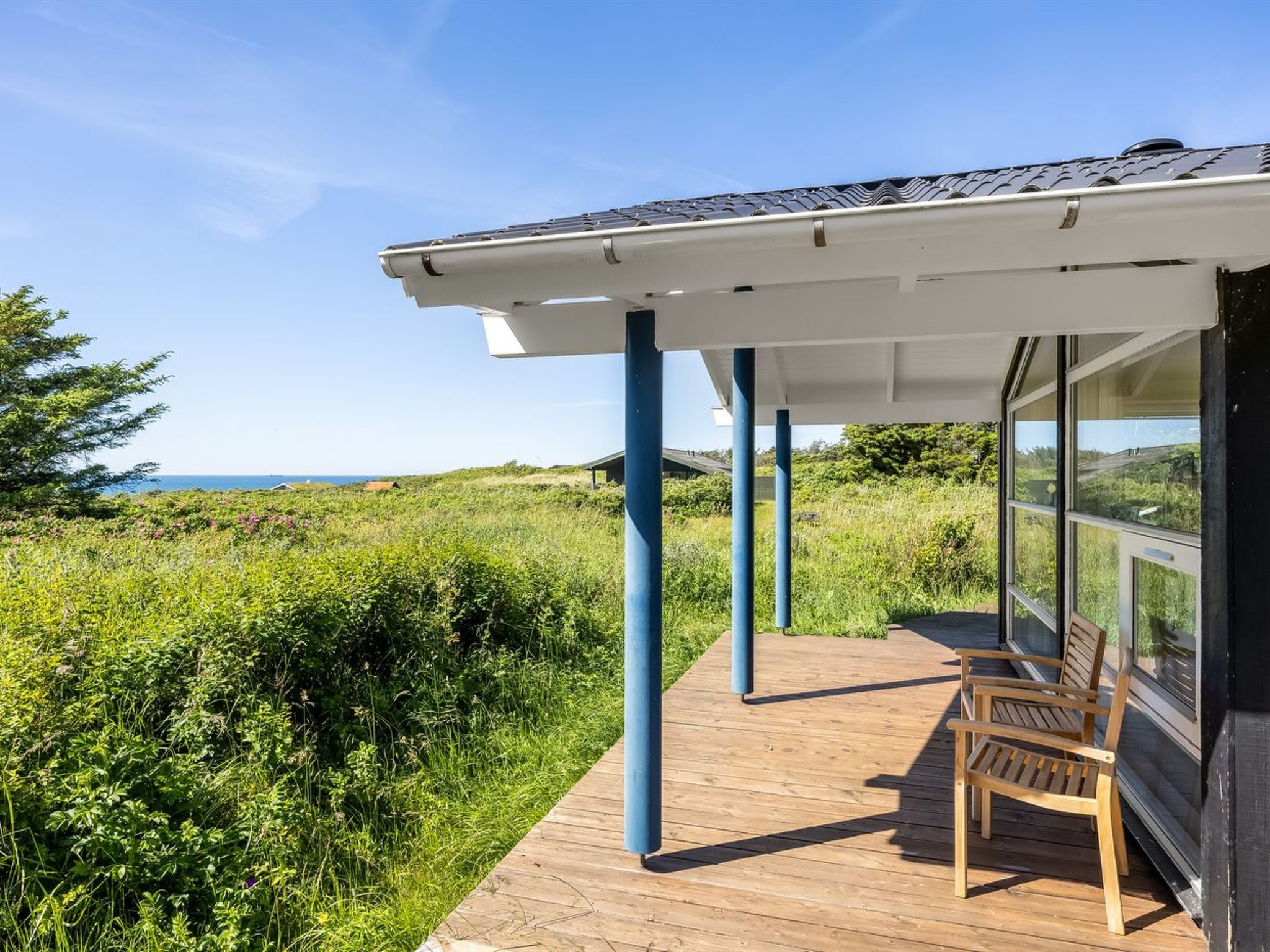 Una terraza de madera con zona cubierta, con vistas a un paisaje cubierto de césped y al mar.