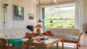 Sala de estar com dois sofás, uma mesa de centro de vidro e uma grande janela com vista para o verde.