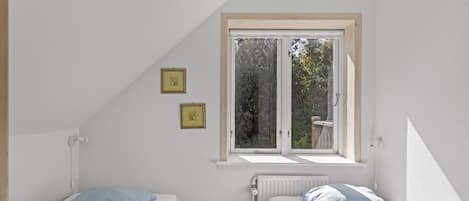 Un dormitorio con dos camas, una ventana con vistas a árboles y un radiador.