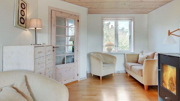 Ein gemütliches Wohnzimmer mit Holzboden, Kamin, Sofa, Sessel und einem Fenster mit Blick ins Grüne.