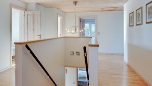 Ein geräumiger Innenraum mit einer Holztreppe, einem Chandelier und gerahmten Kunstwerken an den Wänden.