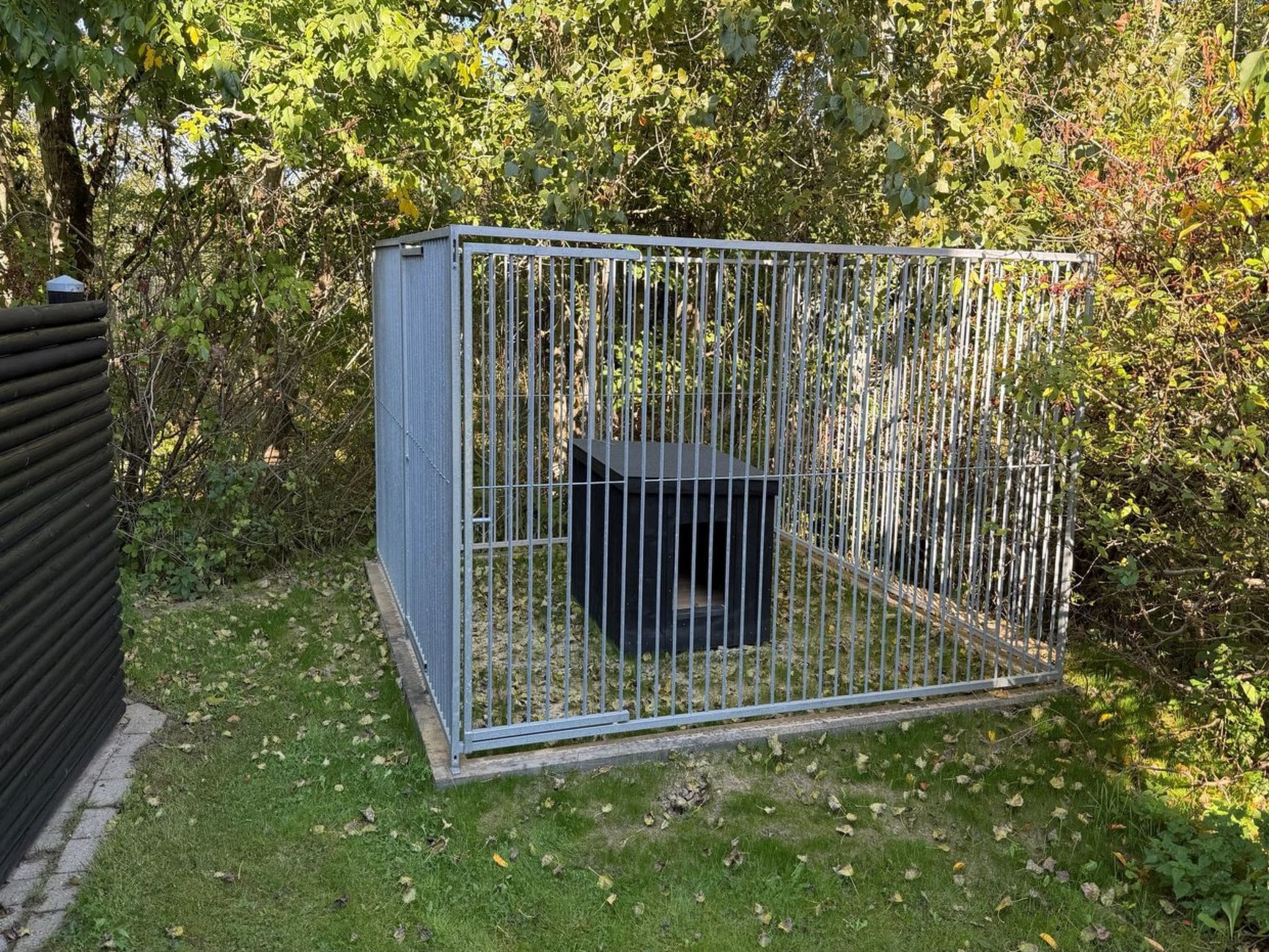 Une structure en métal en forme de cage, située dans un jardin, avec de l’herbe et des arbres en arrière-plan.
