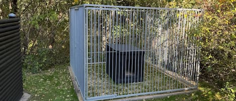 Een metalen kooi-constructie in een tuin met gras en bomen op de achtergrond.