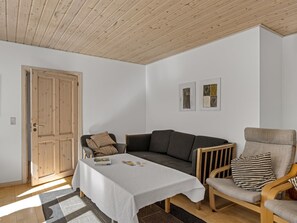 A room with a wooden door, a grey sofa, a wooden armchair, a small table with a white tablecloth, and two framed pictures on the wall. - "Etta" - 957m from the sea by Interhome (Hirtshals)