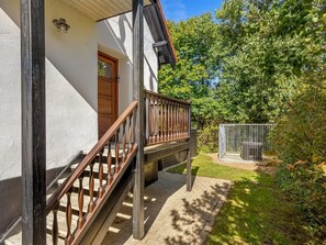 Ein Haus mit einer Holztreppe, die zu einer Veranda, einer Tür und einem eingezäunten Garten führt.