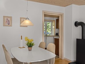 Ein Essbereich mit einem weißen Tisch, Stühlen, einer Hängelampe und einem Topfpflanzen.