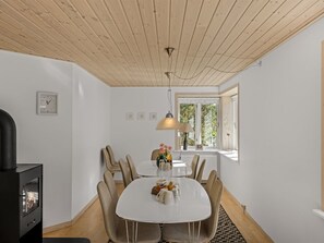 A modern dining area with a round table, six chairs, a black wood-burning stove, and a window with a view of greenery. - "Etta" - 957m from the sea by Interhome (Hirtshals)