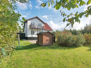 Ein zweistöckiges Haus mit Balkon, einer kleinen Holzhütte und einem gepflegten Rasen.