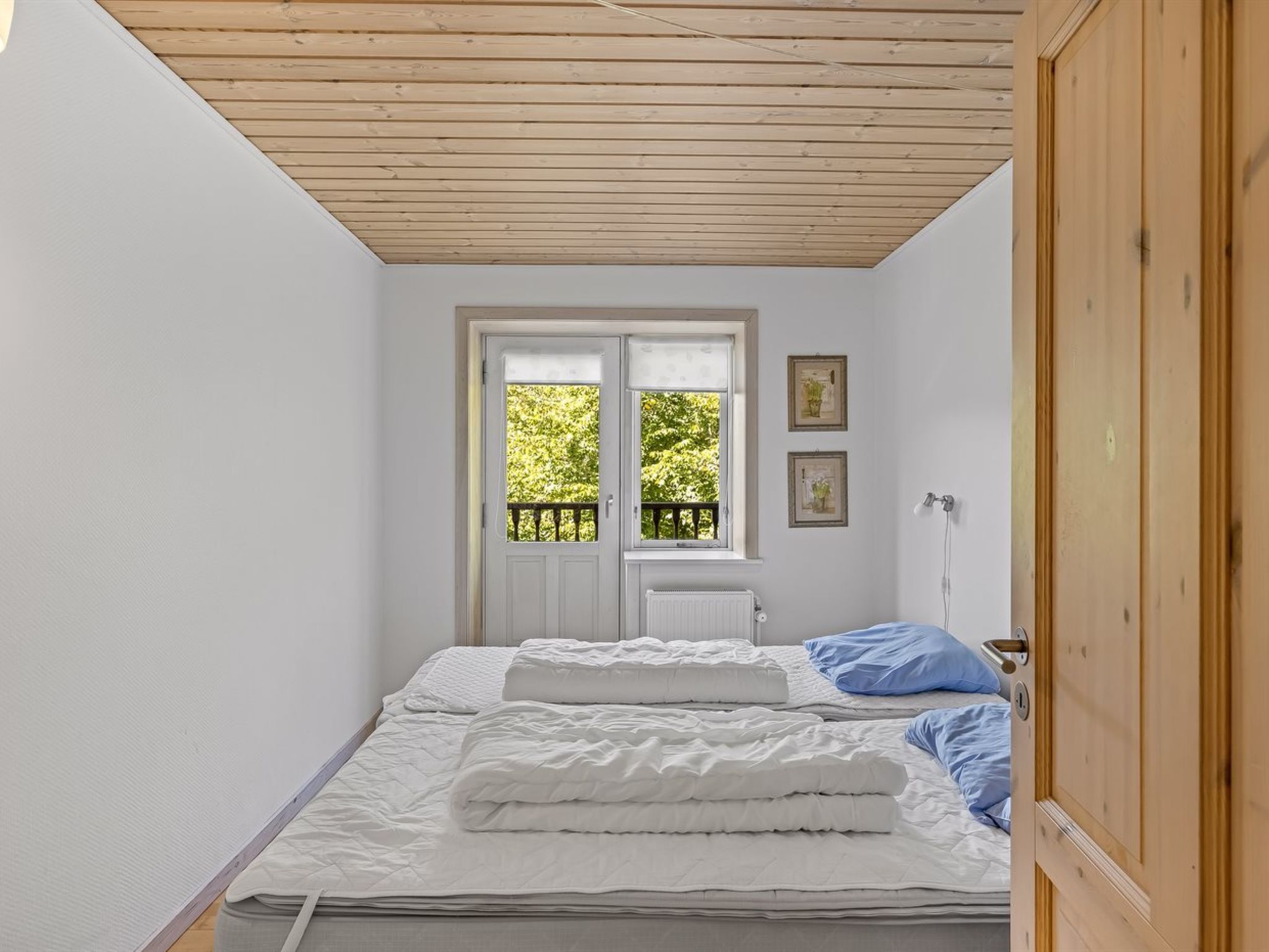 Quarto com cama, janela vista para vegetação e radiador.