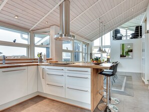 A modern kitchen with white cabinets, a wooden countertop, and a stainless steel range hood. There are large windows providing natural light and a view of the outdoors. - "Rodna" - 452m from the sea by Interhome (Hirtshals)