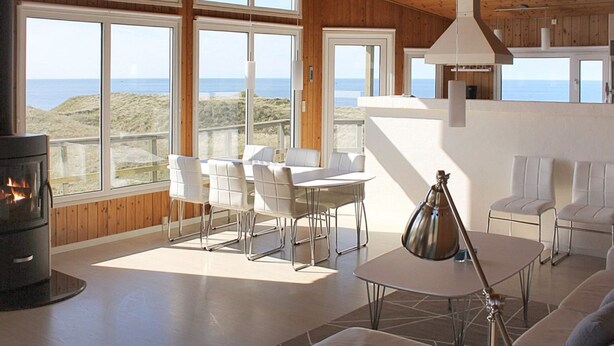 Ein großzügiger Wohnbereich mit großen Fenstern, einem Kamin und Blick auf das Meer.