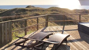 Eine Holzterrasse mit zwei Liegestühlen mit Blick auf einen Strand mit Dünen und dem Meer.