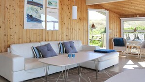 Ein modernes Wohnzimmer mit einem weißen Sofa, einem runden Tisch und Blick auf einen Garten durch eine Glasdoor.