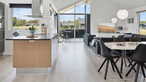 A modern kitchen with a central island, a dining area with a table and chairs, and a living area with sofas.
