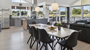 A modern kitchen with a dining area, large windows, and a view of the outdoors.