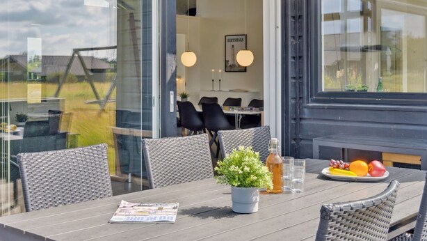 An outdoor dining area with a table, chairs, a potted plant, and a plate of fruit.