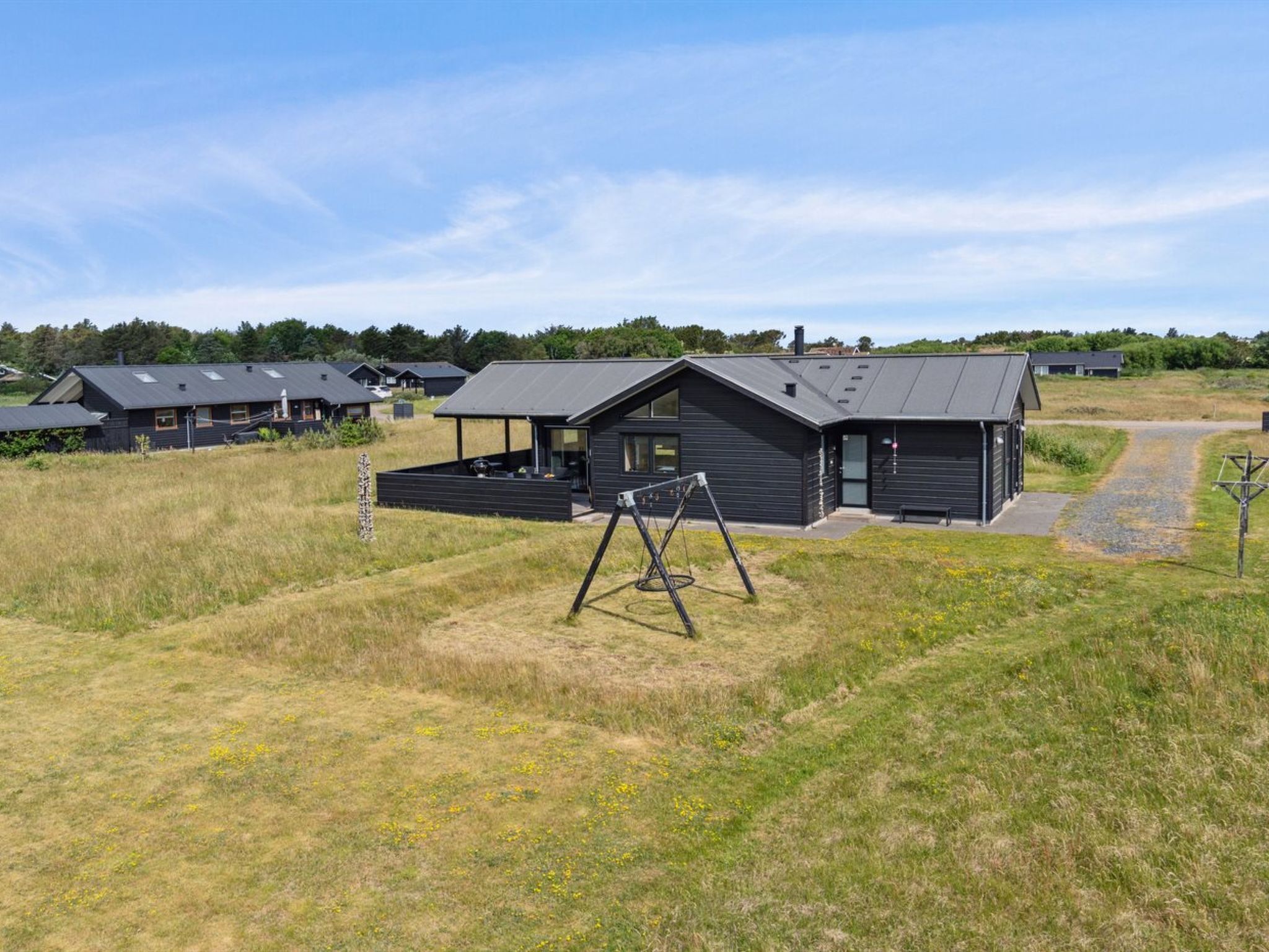 A modern building with a flat roof and large windows, surrounded by open grassy fields and other similar buildings.