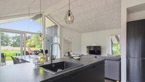 A modern kitchen with a large island, a dining area with outdoor seating, and a living room with a large TV.