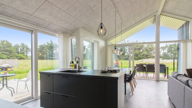 A modern kitchen with a large island, large windows, and a view of the outdoors.