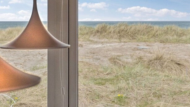 Una stanza con una grande finestra vista spiaggia, dune e mare.