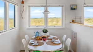Zona pranzo con tavolo apparecchiato per quattro persone, una pianta in vaso e vista sull'esterno.