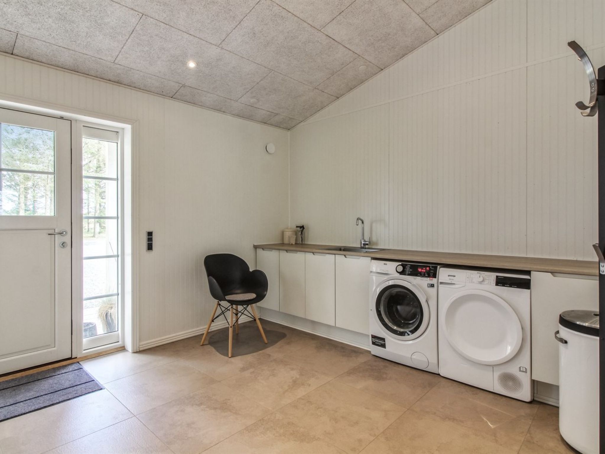 Un cuarto de lavandería con lavadora, una silla y un lavabo.