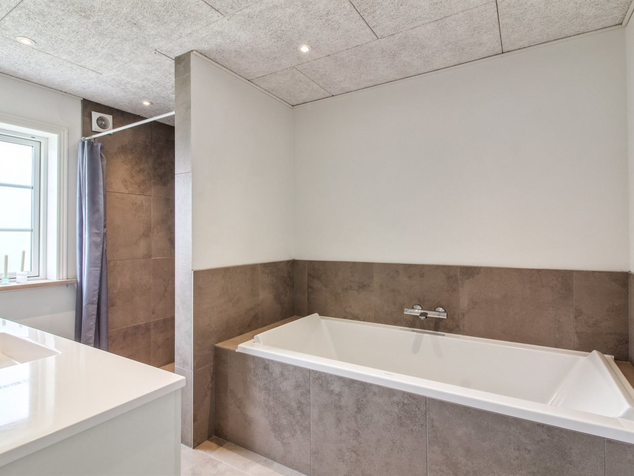 Une salle de bain moderne dotée d’une baignoire îlot, d’un espace douche et d’une grande fenêtre laissant entrer la lumière naturelle.
