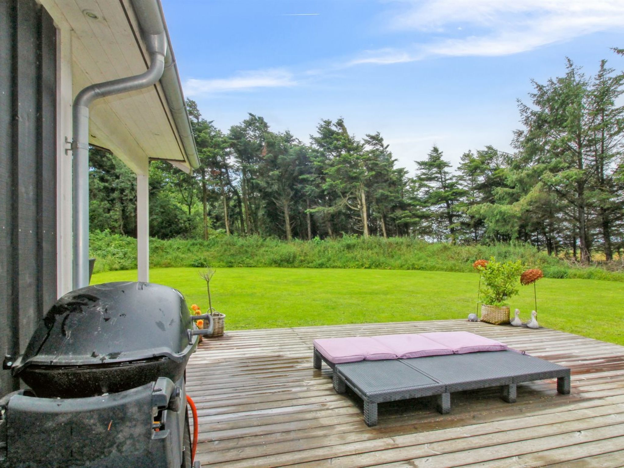 A wooden deck with a grill, a lounge chair, and a small table.