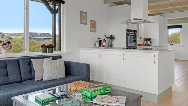 A modern kitchen with white cabinets, a central island, and a dining area with a glass coffee table.