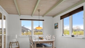 A dining area with a table, chairs, a hanging light fixture, and windows with a view.