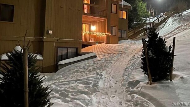 A wooden building with a balcony and a covered entrance, surrounded by snow.