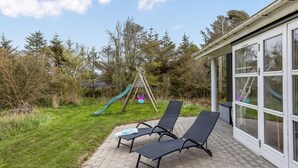 A patio with two lounge chairs, a wooden swing set, and a glass-enclosed building. - "Hauke" - 478m from the sea by Interhome (Hjørring)