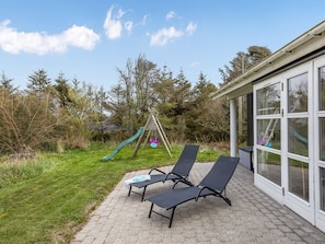 A patio with two lounge chairs, a wooden swing set, and a glass-enclosed building.